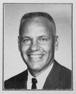 Black and white photograph of Principal Robert F. Jarecke. He is wearing a dark suit and tie and is smiling broadly. 