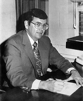 Black and white photograph of Principal David L. Meadows from a Marshall Road yearbook. He is seated at the desk in his office, signing paperwork.  