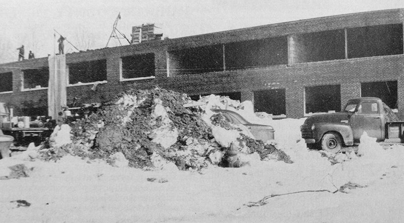 Black and white photograph of Marshall Road Elementary School during construction. The photograph was taken during the winter of 1961 because there is snow on the ground. The shell of the building is in place, but there are no windows. Workmen are visible on the roof. 